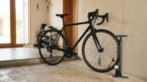 玄関先の壁際に黒いロードバイクが立てかけられ、その横に空気入れ(フロアポンプ)が置かれている朝の様子